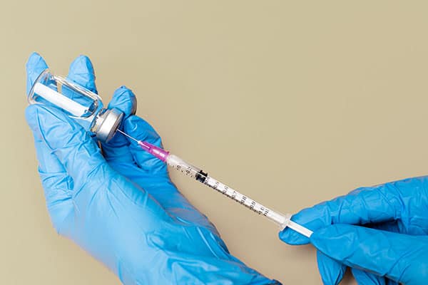 Person wearing blue medical gloves drawing up medication with a syringe